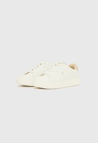 Zapatillas blancas con parte superior de cuero liso, suela plana de goma, puntera redonda, detalles beige en el talón y detalles perforados en los laterales.