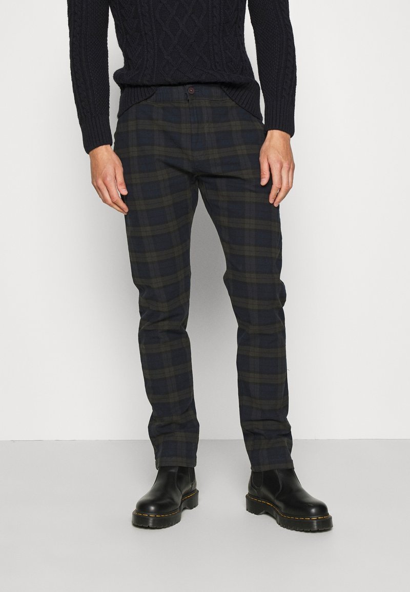 Pantaloni a quadri blu scuro con accenti verdi e grigi. Design slim fit con bottone in vita e tasche laterali. Abbinati a stivali neri.
