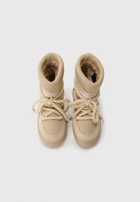Beige ankle boots with a rounded toe, padded cuffs, fabric and suede materials, featuring a lace-up design and gold-tone hardware accents.