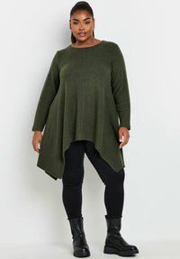 Grön långärmad tunika med en flödande fåll, tillverkad av mjukt material. Bärs över svarta åtsittande byxor och kraftiga svarta stövlar. Enkel rund halsringning.