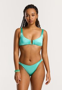 Tirkizni bikini set koji se sastoji od bralete s naboranim središnjim dijelom i širokim trakama, upairan s donjim dijelovima niskog struka i minimalne pokrivenosti. Glatka tekstura.