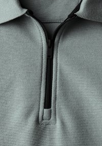 Světle zelený fleece pulovr s půl zipem, který má texturovaný povrch, černý zip a kontrastní límec.