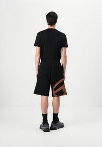 Black t-shirt and shorts with a large brown graphic pattern on the lower left. The shorts have an elastic waistband and pockets. Black socks and shoes.