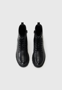 Bottines en cuir noir avec une texture lisse, avant à lacets, bouts ronds et languettes à l'arrière. Fermetures éclair latérales cachées pour un enfilage facile.
