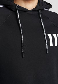 Černá mikina s kapucí s bílým logem "11 Degrees" na hrudi a černými stahovacími šňůrkami s bílým textem.