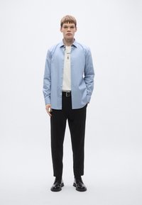 Hele sinine triiksärk, all valge t-särk, mustad püksid ja mustad kingad. Sile kangas, lõdvestunud istuvus, minimalistlik disain.