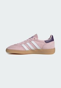 Zapatilla Adidas de ante rosa con rayas blancas, talón morado y suela de goma, mostrada de lado sobre fondo blanco.