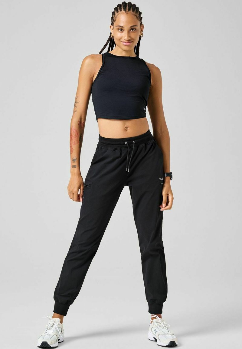 Sort crop-top og sorte joggers med elastiske manchetter, lavet af glat stof. Har justerbar talje og sidelommer. Hvide sneakers.