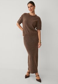 Bruin gebreid twee-delig outfit met een top met korte mouwen en een lange, aansluitende rok. De stof heeft een zachte textuur met een subtiele glans.
