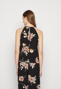 Top haltere floral preto com flores rosas e amarelas, tecido suave e detalhe de costas em forma de fenda. Corte solto com um design em camadas.