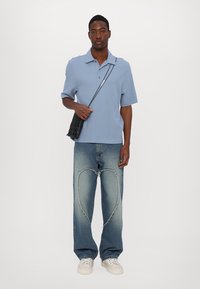 Šviesiai mėlynas trumpas polo marškinėliai, laisvas pakirtimas. Nusidėvėję šviesiai mėlyni džinsai su širdies formos išpjova. Juoda rankinė per petį, balti sportbačiai.