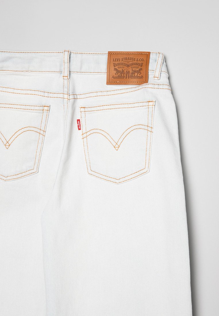 I jeans in denim bianco presentano cuciture arancioni, due tasche posteriori con un design curvo distintivo e una toppa in pelle marrone del marchio sulla cintura.