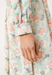 Blommönstrad långärmad klänning med pastellfärger, mjuk textur och manschettdetalj. Designen innehåller gröna, rosa och blå nyanser.