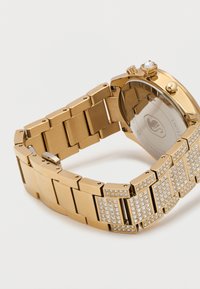 Βραχιόλι ρολογιού από χρυσό μέταλλο με τετράγωνα συνδετικά, διακοσμημένα με μικρά διαυγή κρύσταλλα, προσαρτημένο σε στρογγυλή πίσω πλευρά κάσας ρολογιού.