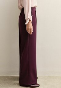 Bordeaux wijd-uitlopende broeken van een gladde stof, met een hoge tailleband en plooien. Gecombineerd met een lichtroze blouse en donkere schoenen.