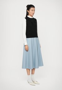 Gilet noir en tricot avec une superposition en texture florale, porté sur une chemise blanche à col, associé à une jupe midi bleu clair et des chaussettes blanches, ainsi que des chaussures à talons pointues crème.