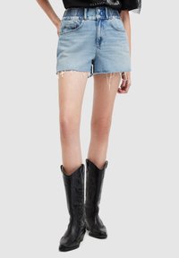 Shorts de mezclilla azul claro con dobladillo deshilachado, de cintura alta y con bolsillos frontales. Combinados con botas de vaquero de cuero negro que presentan diseños en relieve.