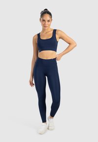 Marinblå atletisk croptopp och högmidjade leggings gjorda av ett mjukt, stretchigt tyg. Modellen bär vita sneakers.