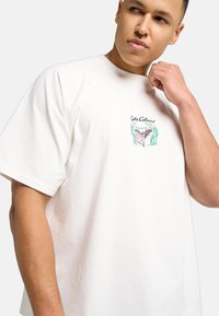 Hvid oversized t-shirt lavet af bomuld med rund hals. Har et grafisk print på brystet med blomsteraksenter og en afslappet pasform.