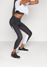 Svartvita aktiva leggings med hög midja, slät yta och paneldetaljer. Kombinerad med svarta sportskor för kontrast.