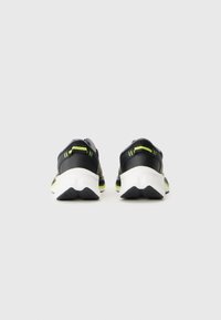 Sapatos de desporto pretos com detalhes verdes, apresentando uma sola texturizada e acolchoada e um design aerodinâmico. A vista traseira destaca a forma única.