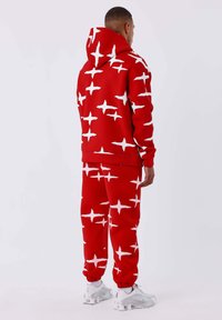 Rode hoodie en bijpassende broek van zachte stof, met een wit sterrenpatroon. Elastische mouwen en zoom, met een trekkoord in de capuchon.