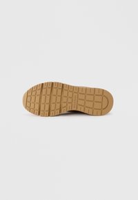 Semelle de sneaker Skechers, avec une surface en caoutchouc texturé et un motif en grille. La couleur est beige avec un détail de logo en relief.