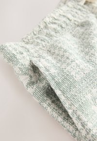 Gros plan sur un tissu texturé avec un motif tissé en vert clair et blanc, montrant des plis et des détails de couture.