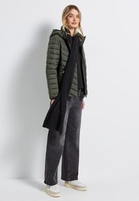 Grön puffjacka med huva och dragkedjefickor, kombinerad med svarta jeans och en lång svart halsduk. Vita och beige sneakers fulländar looken.