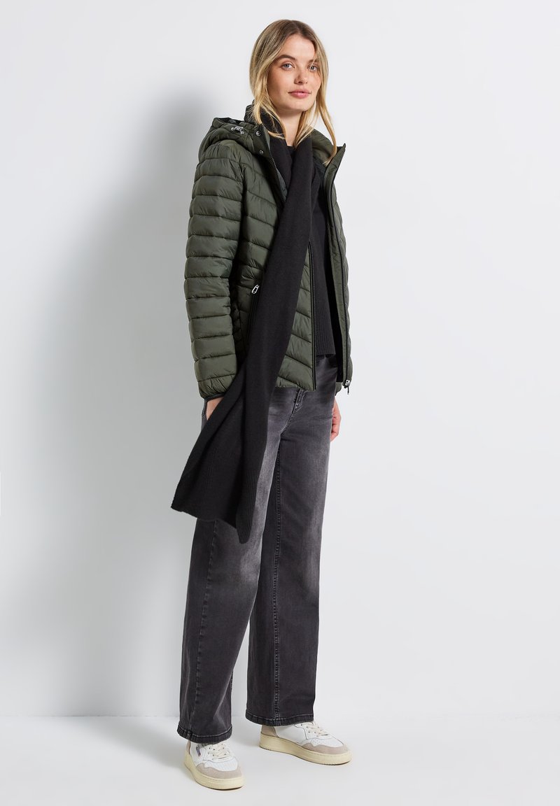 Grön puffjacka med huva och dragkedjefickor, kombinerad med svarta jeans och en lång svart halsduk. Vita och beige sneakers fulländar looken.