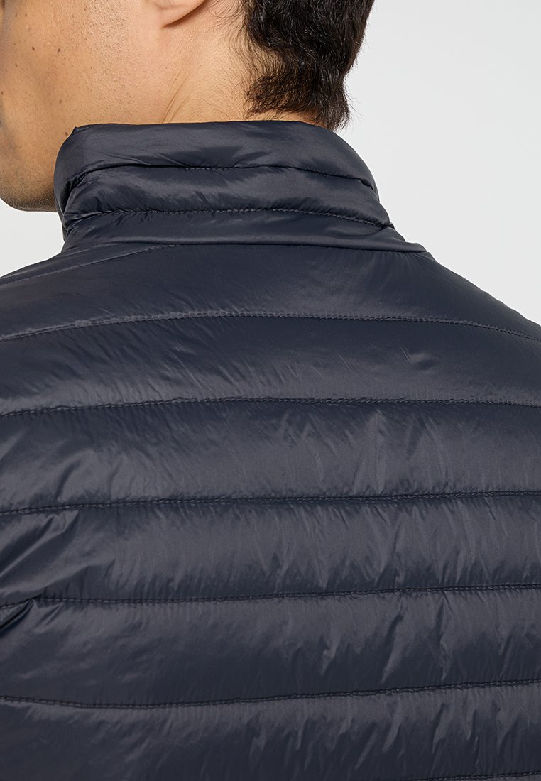 Giacca in piuma blu navy con design trapuntato, colletto alto e materiale leggero. Texture liscia con dettagli di cucitura orizzontale.