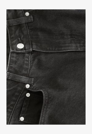Black denim fabric features a textured surface, with silver snap buttons and a zipper at the side, showcasing a structured design.