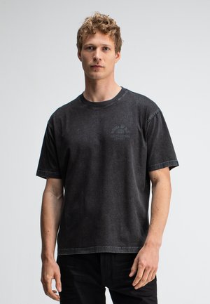 Zwarte T-shirt met korte mouwen en een licht vervaagde textuur, voorzien van een klein circulair logo op de borst en zichtbare stiksels.