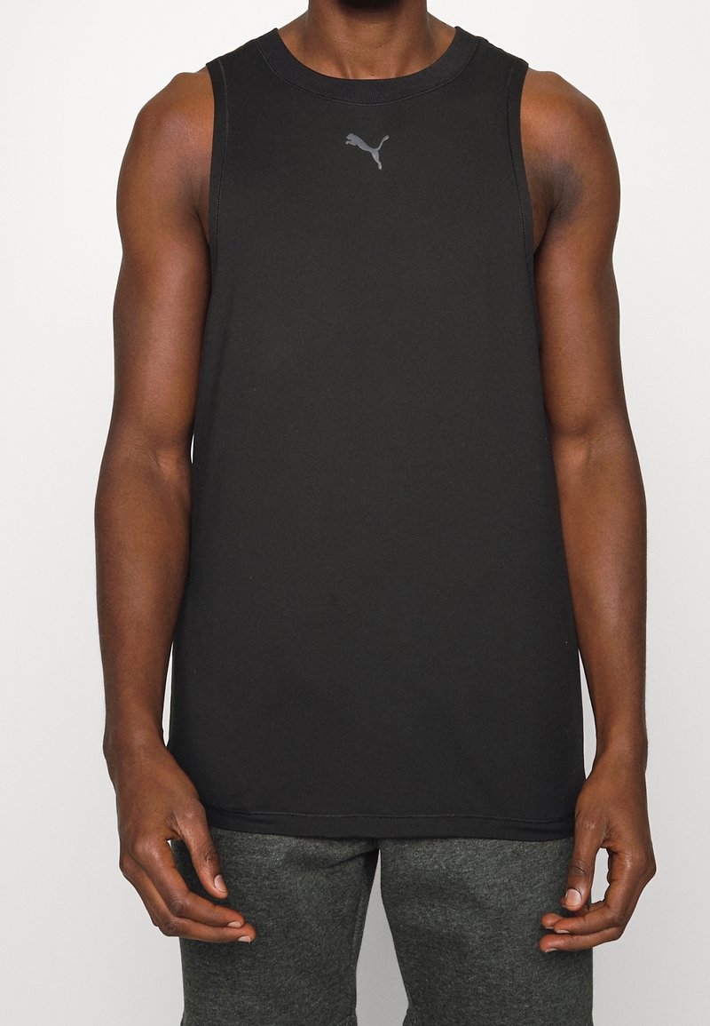 Débardeur sans manches noir en tissu, avec un col rond et un petit logo gris sur la poitrine. Porté avec un pantalon gris.