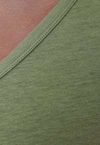 Grønt bomuldsstof med en v-hals-design, glat tekstur og fine ribbede detaljer langs halsudskæringen, set i nærbillede.