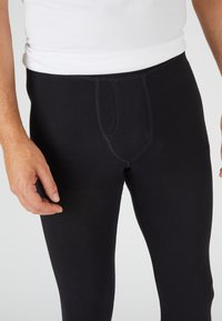 Leggings elásticos negros con una textura suave y flexible, y una apertura de bolsillo en la parte delantera. La cinturilla presenta un borde cosido simple.