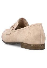 Beige suede slip-on shoe with a flat brown sole. Features a stitched design and an embossed logo on the side. Soft, textured finish.