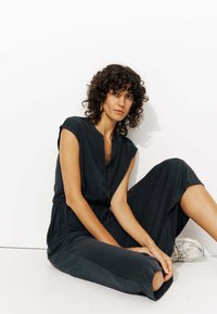 Combinaison noire à manches courtes avec un devant boutonné, une taille cintrée et une coupe ample. Le tissu lisse drape élégamment le corps.