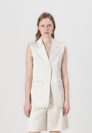 Blazer sin mangas color crema con solapas de muesca, bolsillos frontales y aberturas laterales, combinado con pantalones cortos color crema a juego. Tejido suave y ajustado.