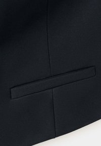 Gros plan d'un tissu noir avec une poche passepoil horizontale et un détail de couture verticale sur un vêtement.