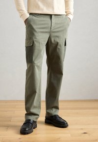 Zelené cargo kalhoty z bavlněné směsi, s bočními kapsami, volnějším střihem a rovnými nohavicemi. Doplňují je černé loafers.