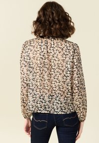 Blusa trasparente con motivo floreale nei toni del rosa, bianco e nero. Presenta maniche lunghe, dettagli arricciati al collo e una vestibilità ampia.