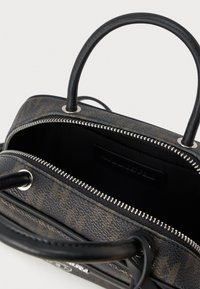 Czarna i brązowa torebka w wzory z metalowym suwakiem częściowo otwartym, ukazującym pustą czarną tkaninę wewnątrz oraz dwie zaokrąglone czarne uchwyty.