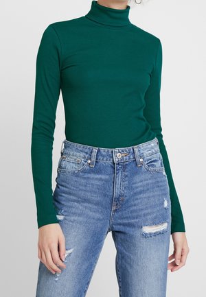 Grøn, ribbet polo trøje parret med lyseblå, slidte jeans med rifter og en høj talje. Lange ærmer, tætsiddende pasform.