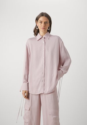 Light pink button-up shirt with a classic collar, long sleeves, and ties at the cuffs. Smooth texture with a relaxed fit.