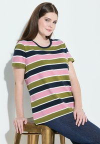 Camiseta de rayas en verde, rosa y azul marino con manga corta, escote redondo y corte relajado. Combinada con unos vaqueros azul oscuro.