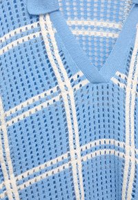 Lys blå strikket sweater med V-udskæring, der har et mønster af hvide striber og åben mesh tekstur.