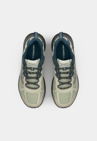 Jasnozielone sneakersy na świeżym powietrzu z siateczkowej tkaniny, wyściełanym kołnierzem i ciemnoniebieskimi akcentami. Posiadają elastyczne sznurowadła i teksturowaną gumową podeszwę.