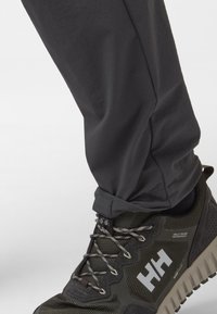 Ciemnoszare lekkie spodnie o prostym kroju, w zestawieniu z chropowatymi czarno-zielonymi butami trekkingowymi z solidną podeszwą i odblaskowymi sznurówkami.