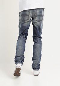 Haaleansiniset farkut, jotka ovat kapeat istuvuudeltaan, viisi taskua ja hienovarainen kulutuskuvio. Yhdistetty valkoisiin tennareihin, joissa on kuvioitu pohja.